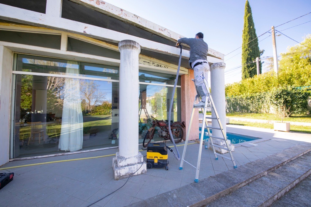 Artisan sur un escabeau utilisant un outil de pon�age reli� � un aspirateur pour la pr�paration et la r�novation d'une fa�ade ext�rieure � Gardanne